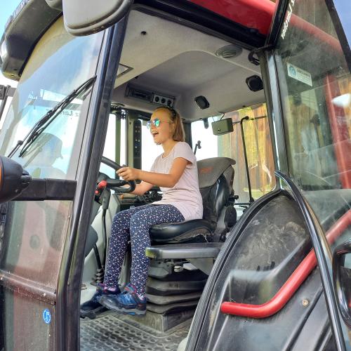 Mädchen sitzt lachend auf dem Fahrersitz eines Traktors